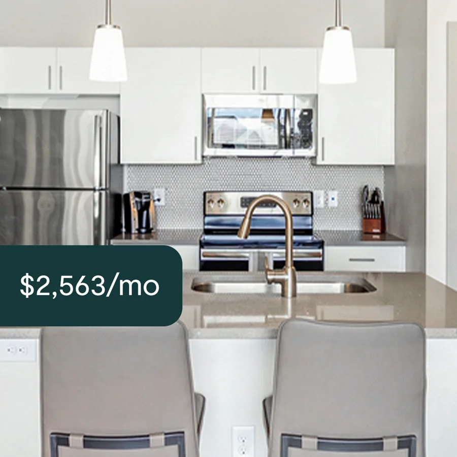 A square ad: a white kitchen with pendant lights, a steel range and two grey stools at the counter, a dark tab with the monthly rent.