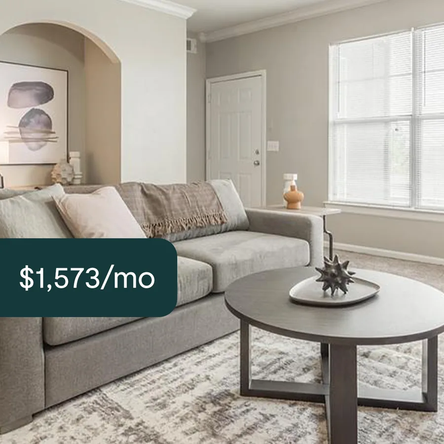 A square ad: a living room with a grey sofa, a round coffee table and an arched alcove, a dark tab with the monthly rent.