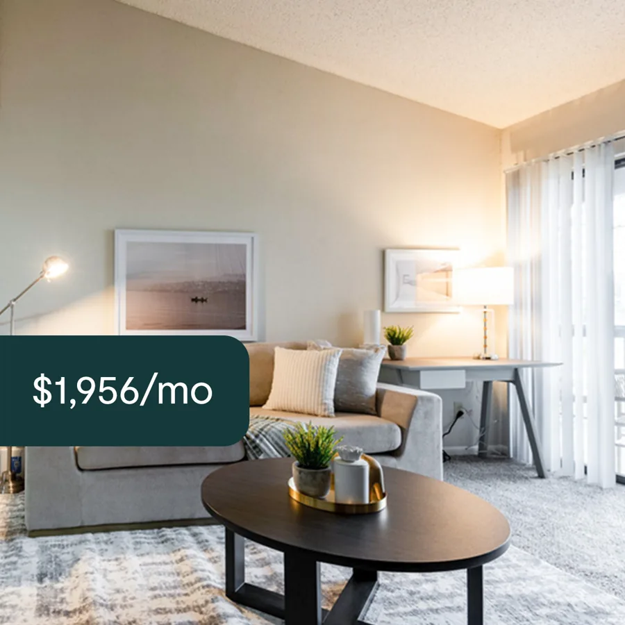 A square ad: a sunlit living room with a sofa, an oval coffee table and a desk, a dark tab with the monthly rent.