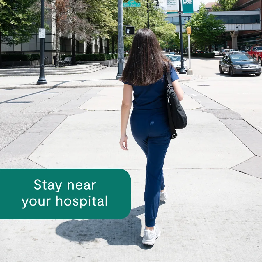 A square ad: a nurse in navy scrubs walks a city sidewalk away from the camera, a green tab reading "Stay near your hospital".