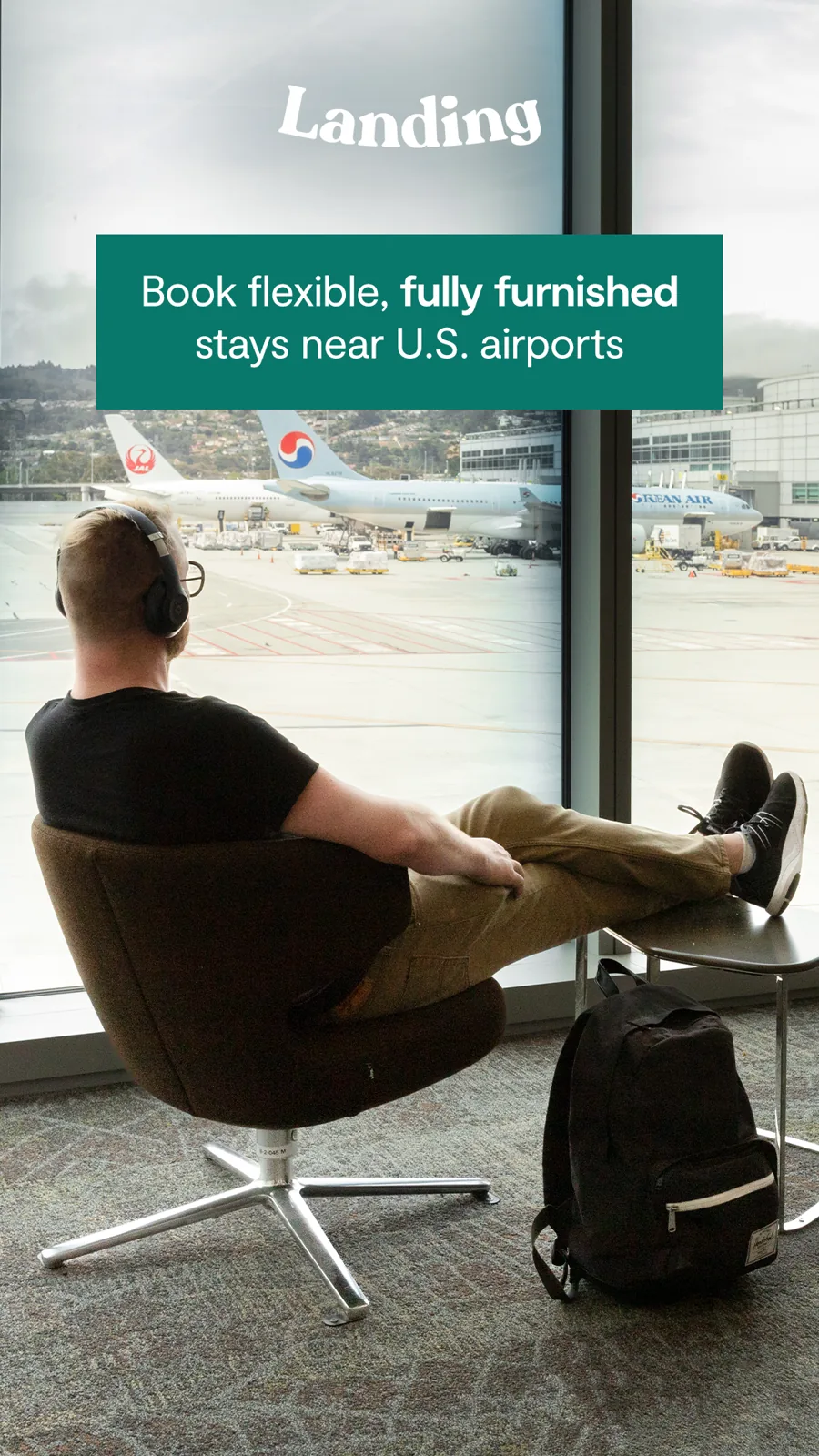 A tall ad: a traveler with headphones rests his feet up by an airport window full of jets, the logo and a green box about furnished stays near airports.